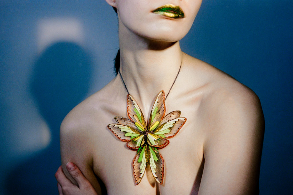 Porté sur peau nue, un imposant collier coloré et translucide, aux allures de papillon hybride
